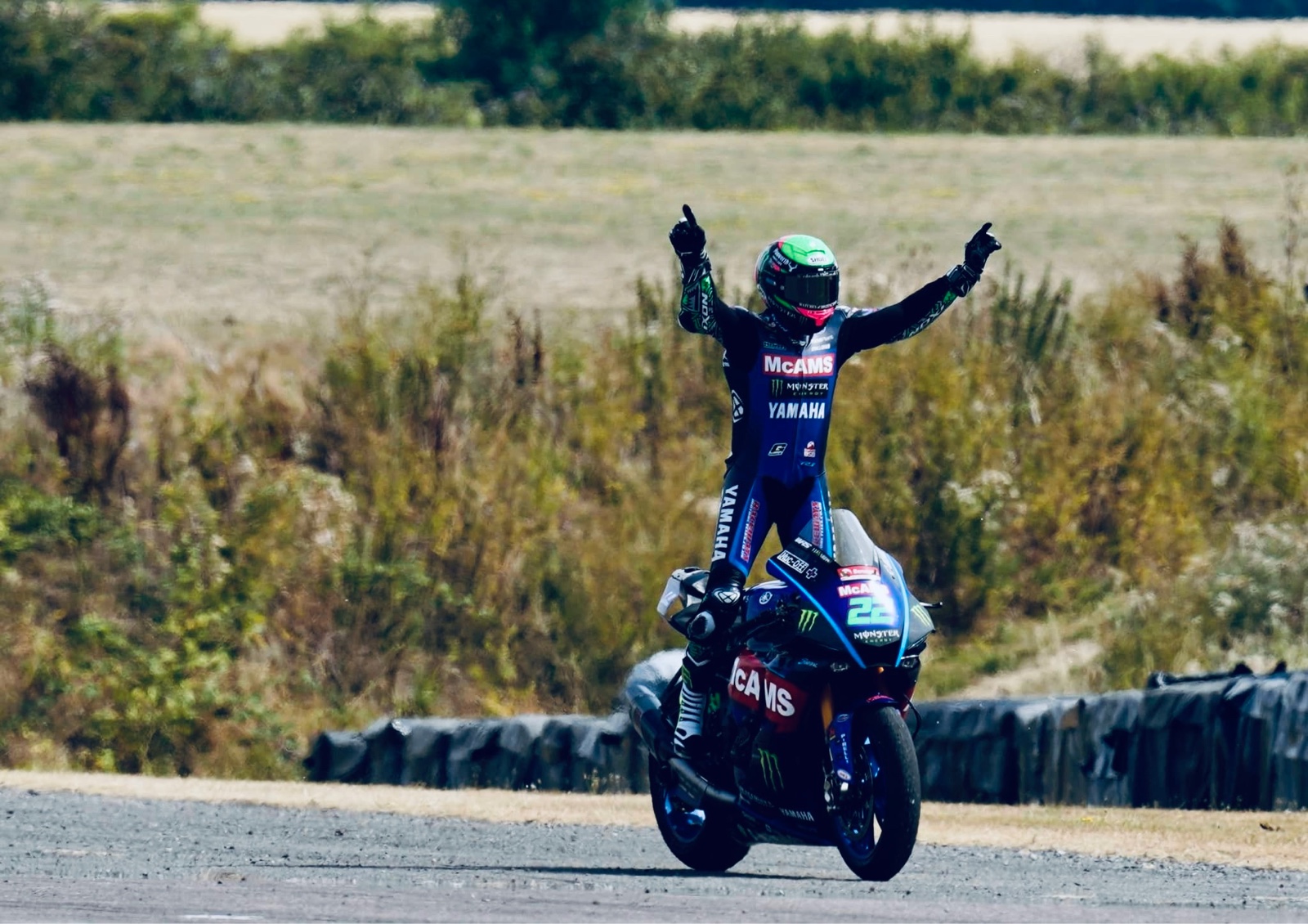 Yamaha Rider standing on a bike with arms inthe air.